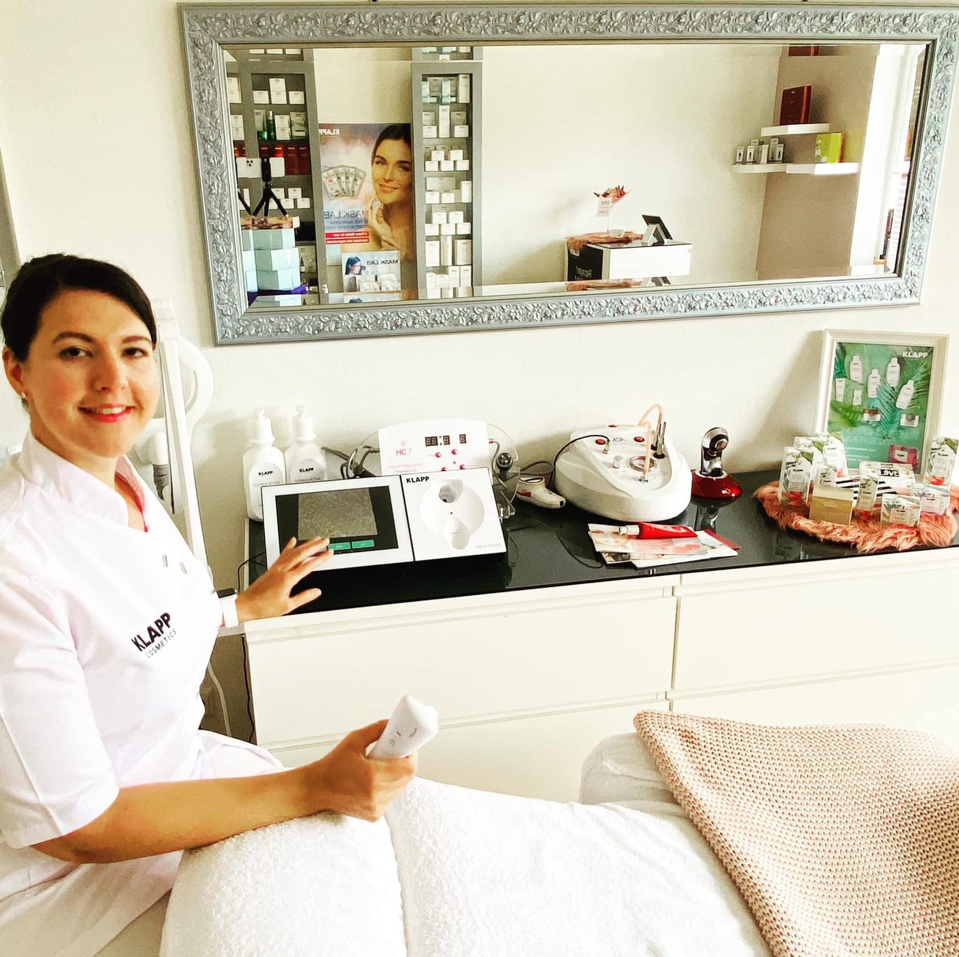 Saskia Kremer-Kastlan sitzt im Hautatelier Kastlan in Merzig neben ihrer Behandlungsliege, im Hintergrund das KLAPP-Hautanalysegerät und weitere apparative Einheiten.
